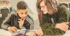 Junger Student hilft einem Schüler beim Lesenlernen