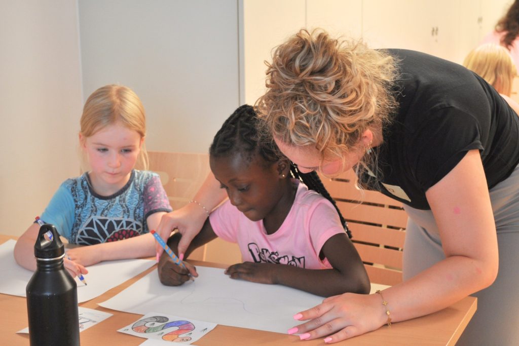 kritzelpatin unterstützt mädchen beim malen im kindergarten