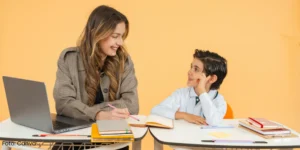 JUnge Frau am Laptop lernt mit Jungen, beide schauen sich an und sitzen jeweils an einem kleinen Tisch